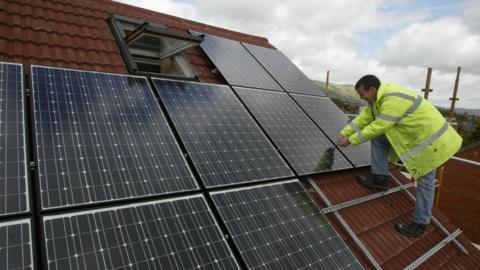 A man in a hi-vis jacket installing solar panels on the roof of a building