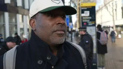 Lance Payne, wearing a baseball cap, stands on a busy Croydon high street 