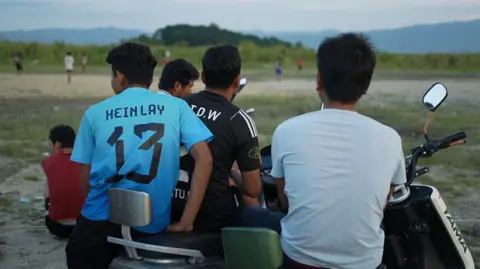 Xiqing Wang/BBC Workers from the factories in Ruili watch while other workers play a game of football  