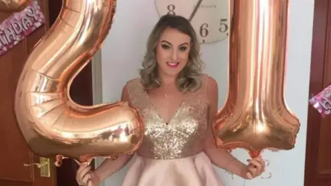 Bethan James with large birthday balloons in shape of numbers one and two wearing sequinned party dress