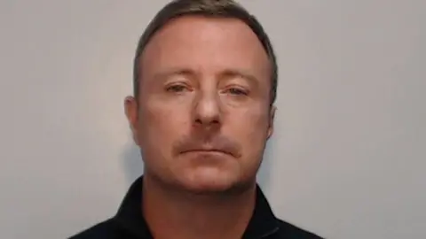 Custody image of Jonathan Cassidy with brown hair and wearing a black shirt.