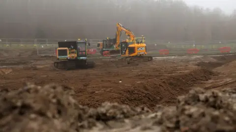 National Highways Two yellow diggers on a muddy site, which is fenced off.