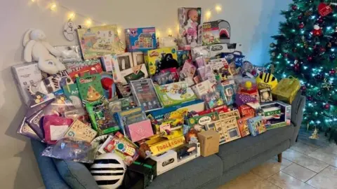 NWAFT Toys and books arranged on a grey sofa, placed next to a green Christmas tree with colourful balls.