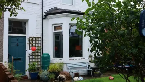 LDRS A house with a bay window, blue door and blue bench outside it.