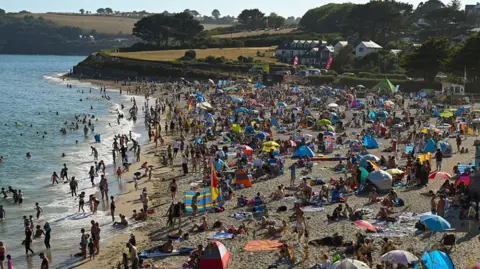 Getty Images Members of the public gather on Gyllyngvase Beach to watch the partial solar eclipse. the beach is pictured to the right while the sea is to the left. The beach is packed with people and the sky is blue above.