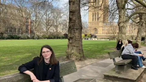 Transportasi untuk semua kepala eksekutif Caroline Stickland duduk di bangku taman dengan Westminster di latar belakang.