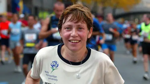 PA Media Late Yorkshire fundraiser Jane Tomlinson is pictured during a run. She is wearing a silver chain with charms on, and a cream t-shirt with the Leeds Metropolitan (now Beckett) University logo on.
