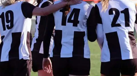 Michael Cook Players from Alnwick Town Ladies club on a football pitch wearing a black and white striped kit. 