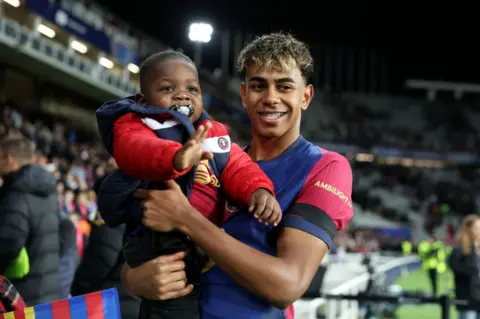 Florencia Tan Jun - UEFA / Getty Images Lamine Yamal Barcelona celebrates victory while holding his brother after the UEFA Champions League 2024/25