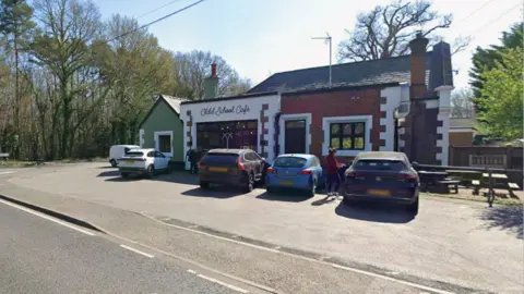 Four vehicles parked outside a single-floor building. The building is split into three colours - green on the left, white in the middle and red on the right. The image is taken from in the road outside the building.