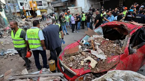 People stand next to a destroyed car, at the site of an Israeli strike in Beirut's southern suburbs, Lebanon September 24, 2024.