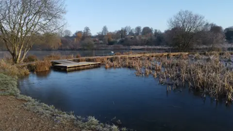 Test Valley Borough Council A dark body of water. There are trees and fields in the background. On the water is a wooden jetty.