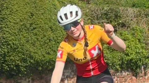HANDOUT A teenage girl in yellow and red cycling gear pumping a fist at the camera - she is wearikng a white helmet and has long red hair in plaits 