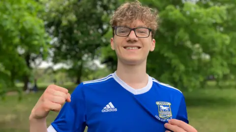 Alice Cunningham/BBC Man in a blue Ipswich Town shirt with his fist raised and clutching at the club's crest on the shirt.