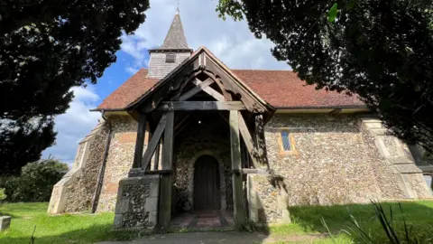Stuart Woodward/BBC A church building sits on grass with trees framing either side. The church has a red tiled roof and stonework walls.