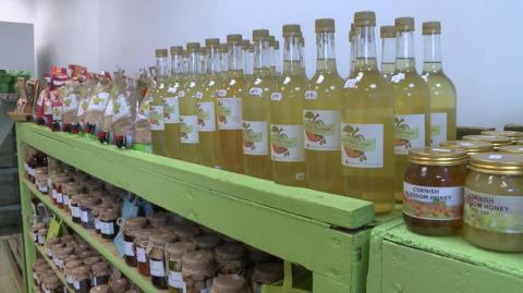 Jars of jam and honey and bottles of apple juice on green shelves 