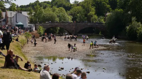 PA Media People ride their horses through the river during the Appleby Horse Fair, the annual gathering of gypsies and travellers in Appleby