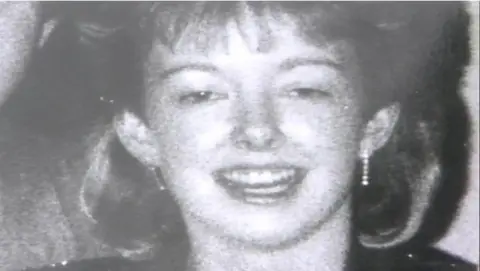 A black and white photograph of Diane Sindall, who has her hair cut into a fringe, smiling at the camera.