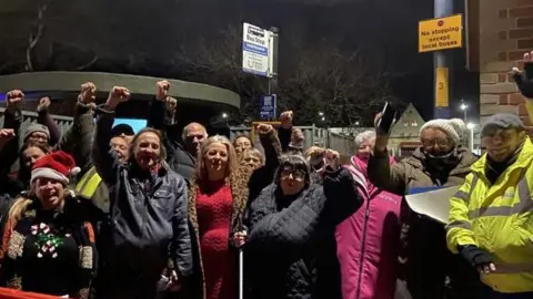 LDRS A group of people all smiling and cheering in front of the bus shelter. 