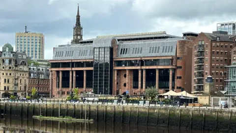 An imposing court buidling made from smooth red-tinged stone and columns, with large dark windows.