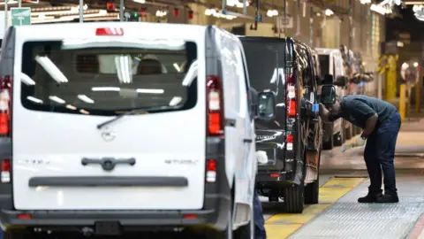 Toby Melville/PA A Vauxhall work inspects a black van on the production line in Luton. The rear of a white van is in the foreground.