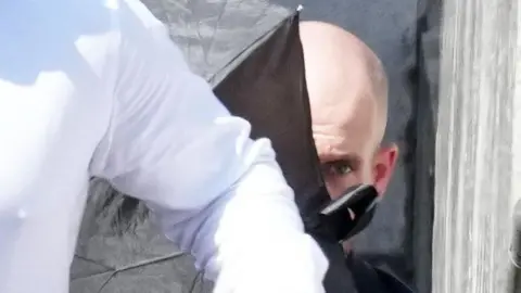 A close-up image of Jake Mullarkey outside court, partially hidden behind a black umbrella.