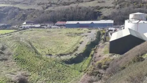 IOM GOV Picture of the silt lagoon near Peel power station. A raised square-shaped bed of grass can be seen alongside houses.