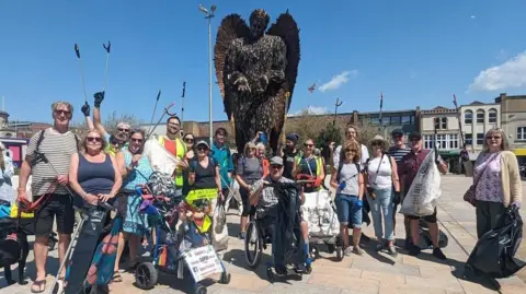 Sophie's super litter picking A large group of litter pickers standing in front of the Weston-super-Mare knife angel. Some are wearing hi-vis vests and others are holding bin bags and litter picking tools