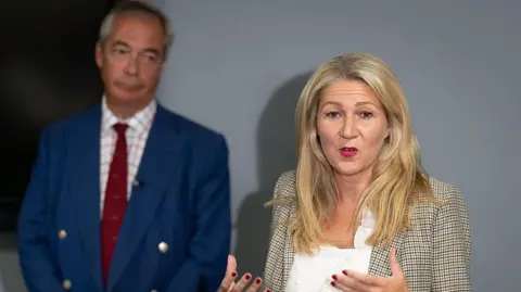 Getty Images Nigel Farage stood in to the left with Laura Anne Jones to the righjtj, in front of a grey background