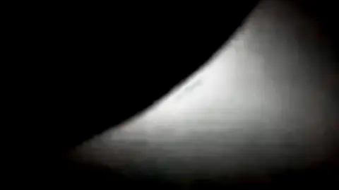 NASA Shimmering white light emerging from a portion of a dark circle in th eblackness of space.