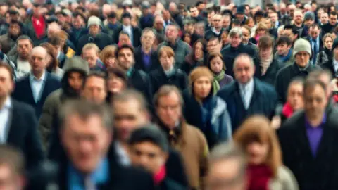 A blurred image of a large crowd of mostly men. Some are wearing shirts and suit jackets and others are wearing coats. Some are also wearing hats or scarves around their necks. 