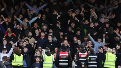 Getty Images Southend United fans singing in a stand. Some have their arms outstretched. In the foreground there are people in security high-vis vests, with their backs turned.