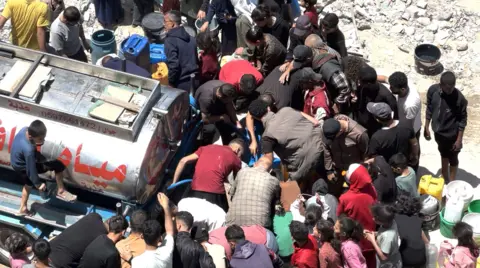 Palestinians scramble to collect water from a tanker in Gaza