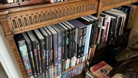 John Devine/BBC A large collection of books, the spines include Elvis in most of them. they sit in an oak style book shelf in the "Elvis room" at the home of Giles Moriarty.