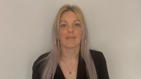 Woman with blonde and purple dyed hair looking directly at the camera against a white wall