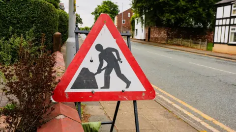 Men at work triangle warning sign on the pavement of an empty road in England.