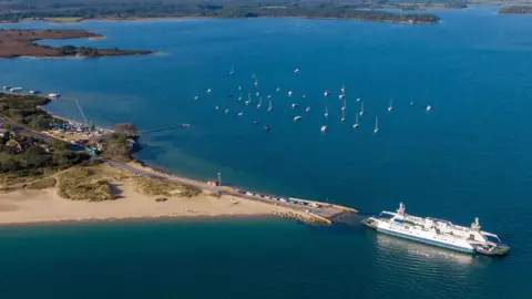Drone view of Poole Harbour with the Sandbanks ferry in the foreground and small boats on the water 