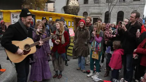 PA Media Glen Hansard wearing a beanie hat and coat busks in Dublin watched by a number of people