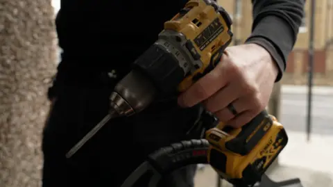 A man's hand is seen holding a large cordless drill