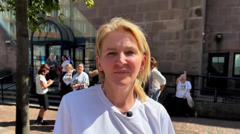 Adele Cook in a white t-shirt standing in front of a large court building
