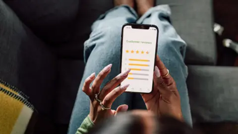 Stock photo shows an overhead view of a person holding a smartphone with a screen saying 'customer feedback' and a star rating interface, as they sit on the sofa at home.