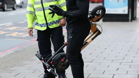 PA Media A man (face not visible) in a black top and black tracksuit bottoms is being stopped by a police officer wearing a high-visibility jacket. 