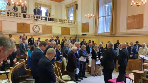Oxfordshire County Councillors in the County Hall chamber have bowed heads during a minute silence.