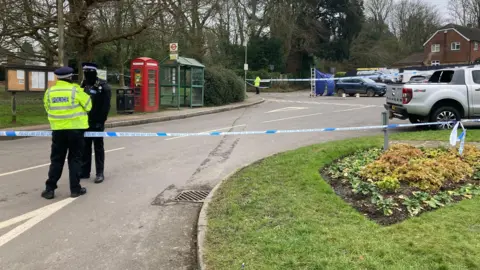 Daniel MacLaren/BBC A road in the village of Knockholt with two police officers and a police tape cordon