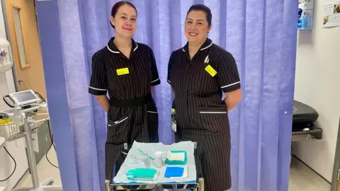 Two female nurses wearing brown and white striped uniforms and standing in front of a tray with cervical screening equipment.