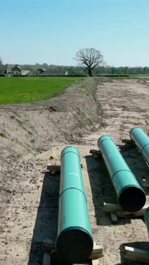 Three green pipes on a muddy part of a field. 