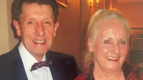 Handout Eddie smartly dressed with bow tie next to his wife. She's blonde with blue eyes and both are smiling happily at the camera.