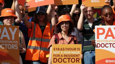 PA Media A crowd of people at the junior doctors protest in England. they are wearing orange and holding signs.
