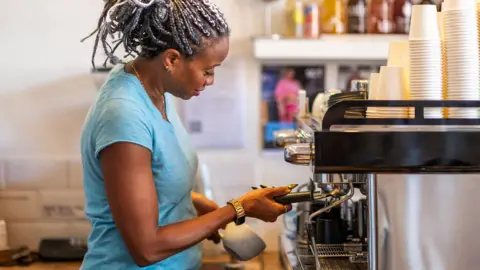 Stock photo shows a barista making coffee at an espresso machine in a coffee shop in the UK