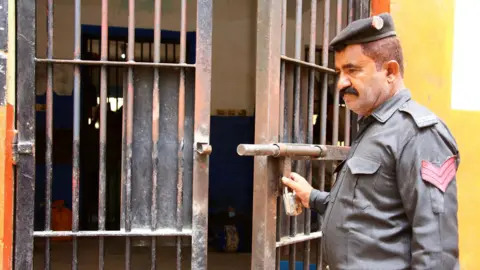 A prison guard stands next to an open cell.